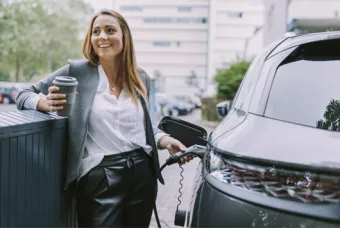 Meisje laad electrische wagen op met koffie in de andere hand